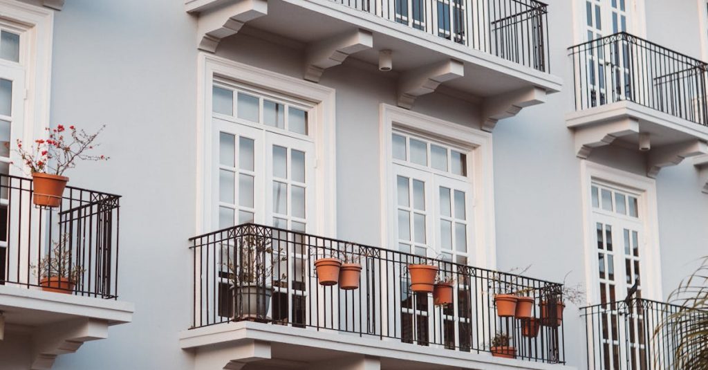 Front view of a modern building with balconies, pots, and white framed windows.