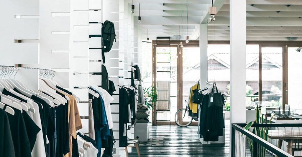 Interior of spacious modern fashion boutique with collection of various clothes hanging on racks in sunlight