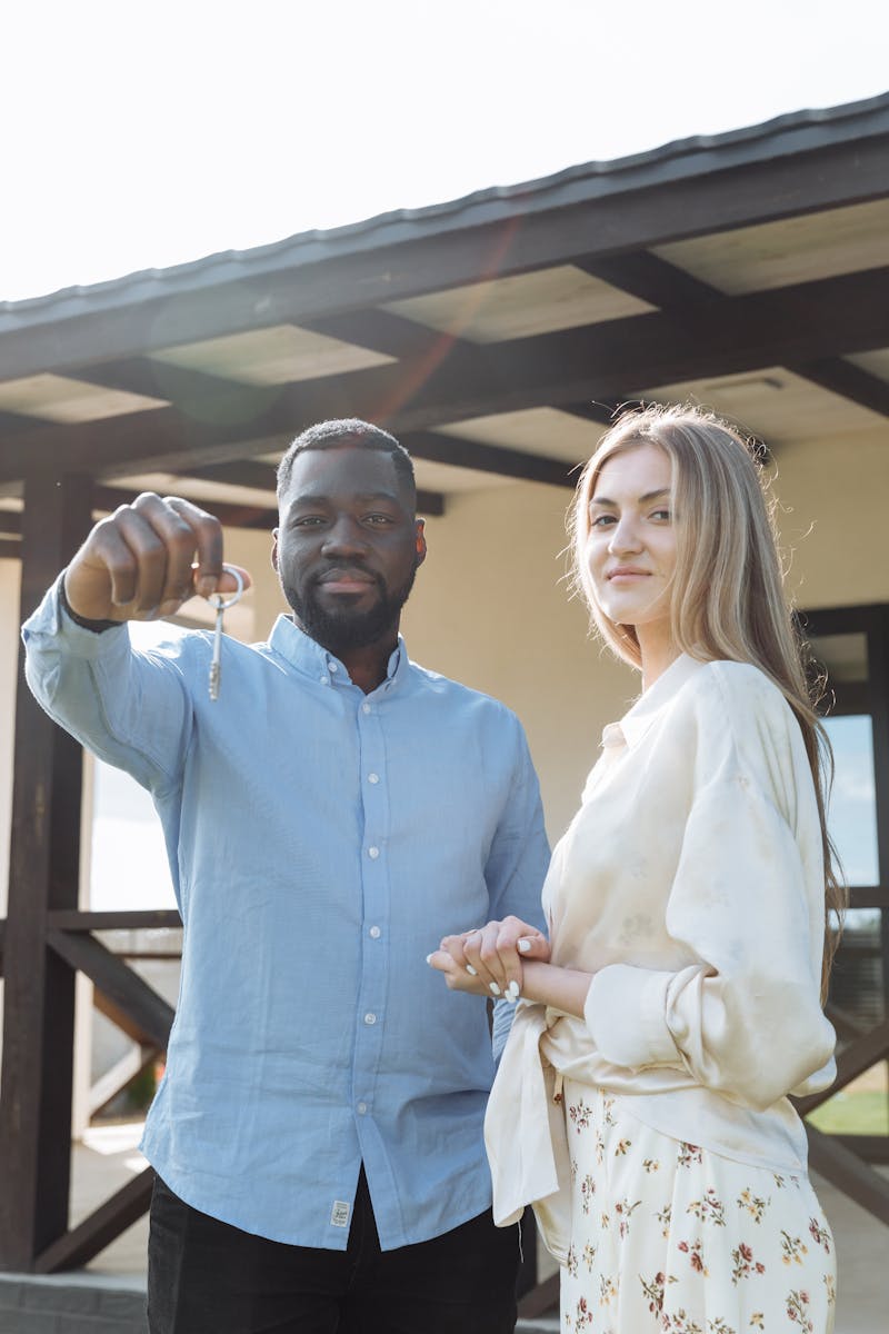 Happy couple holding keys in front of their new home, celebrating their purchase.
