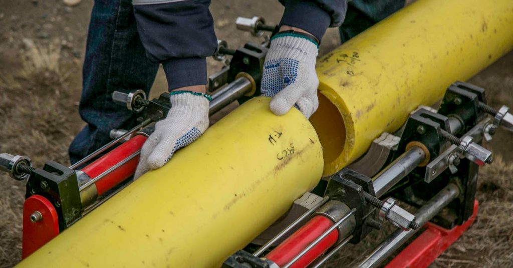 Close-up view of a worker using equipment to install yellow pipes outdoors, focusing on hands and tools.